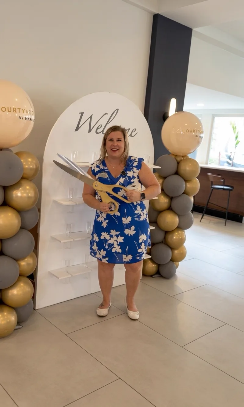 Host beside a white welcome arch with gold and neutral balloons