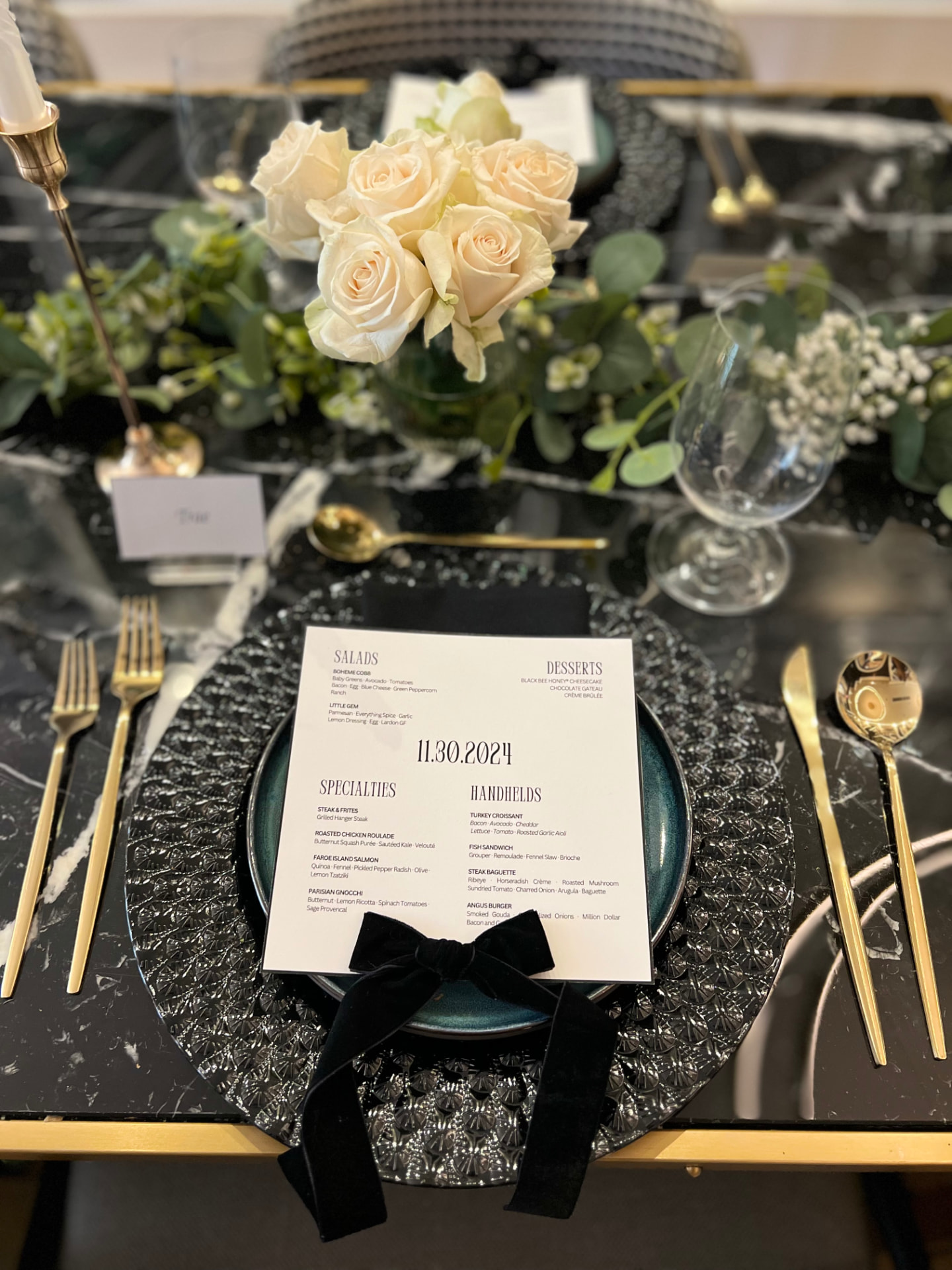 Black and gold place setting with ivory roses and greenery
