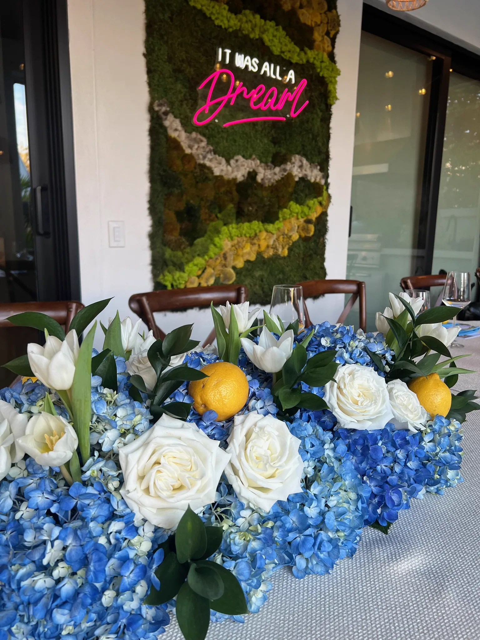 Neon sign on a moss wall above a white and blue floral table runner